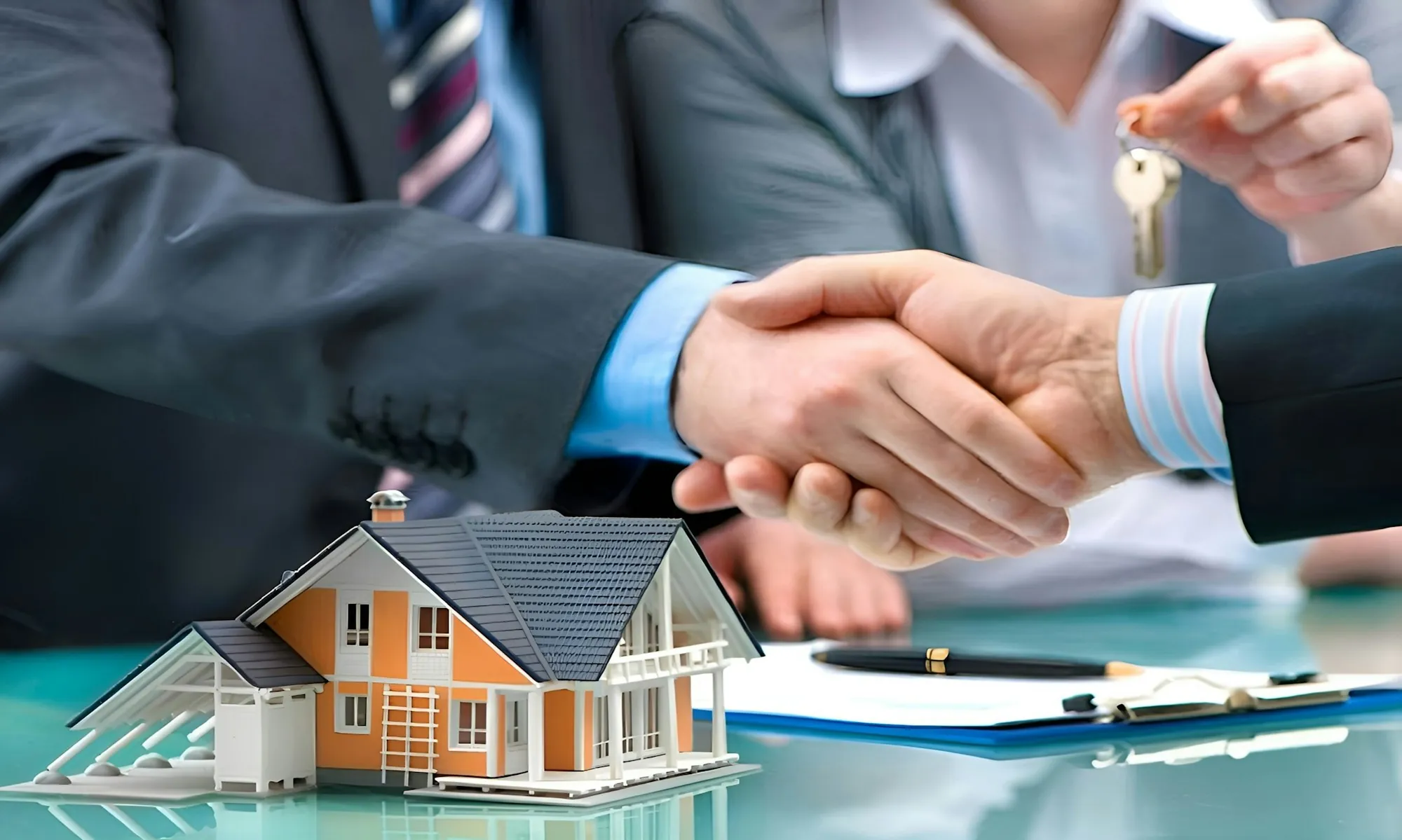 Handshake over a model house and paperwork on a desk