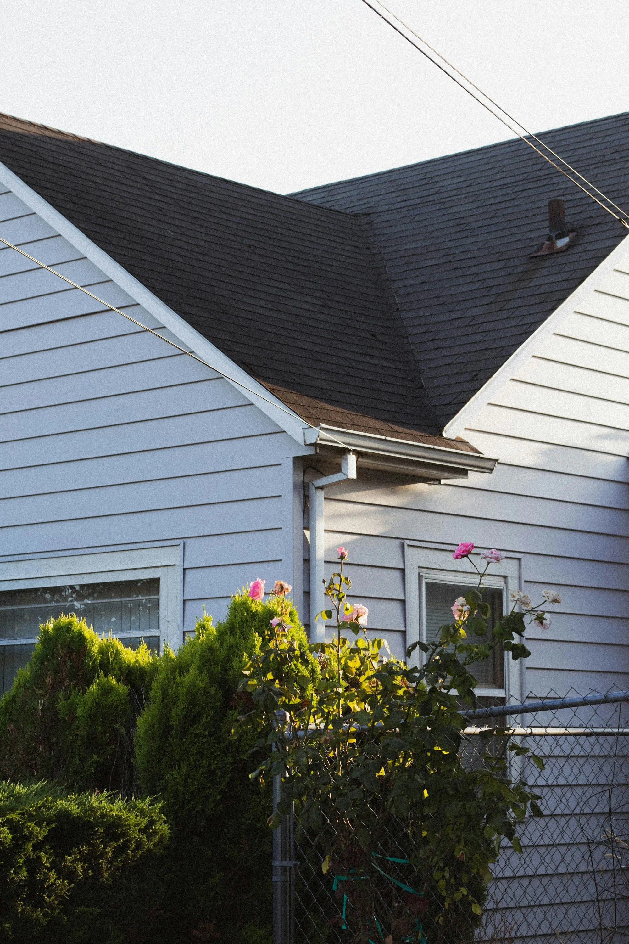 Side of a white-sided home with a shingle gable and flower bed