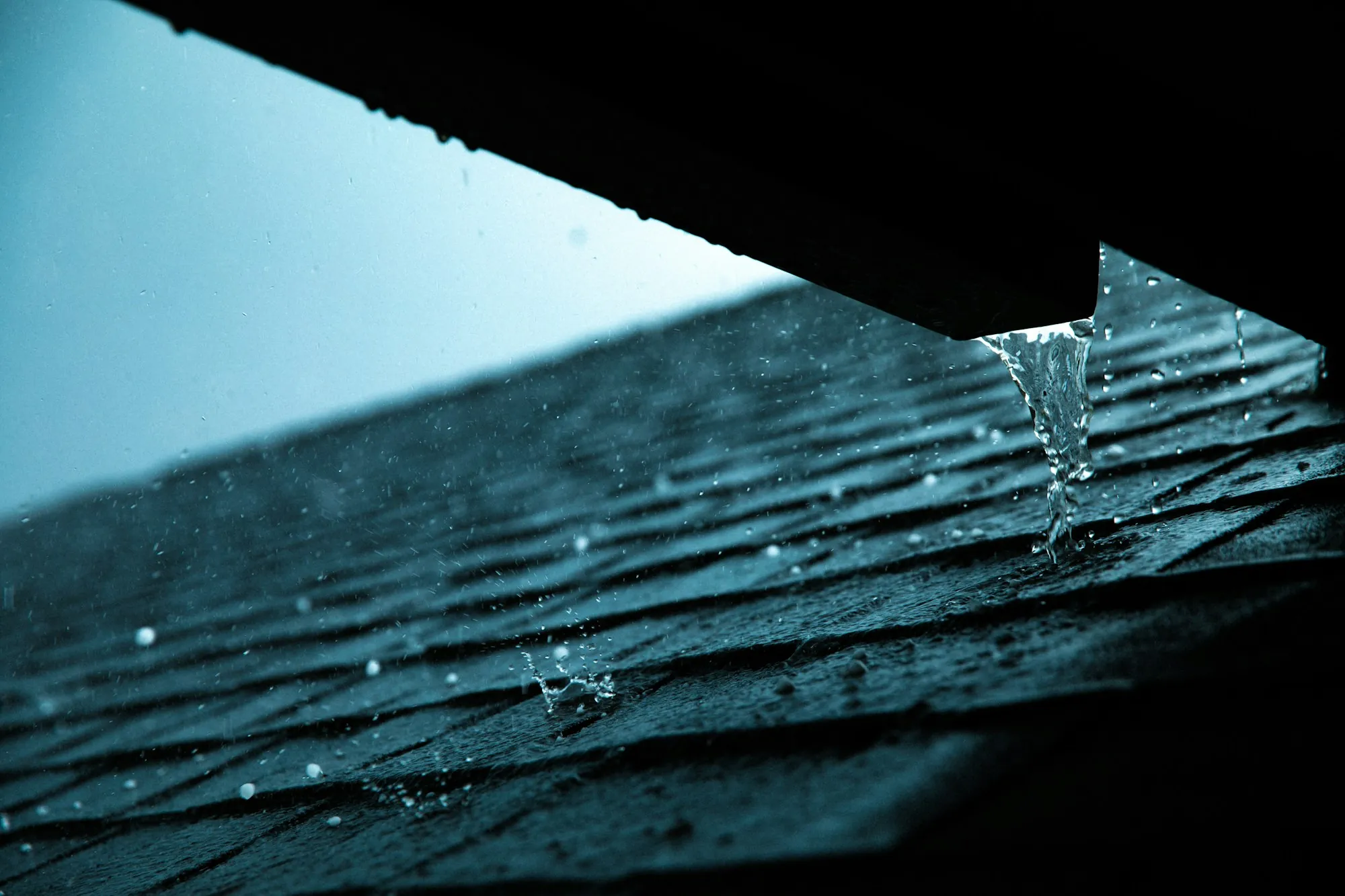 Water dripping off the edge of a wet asphalt shingle roof