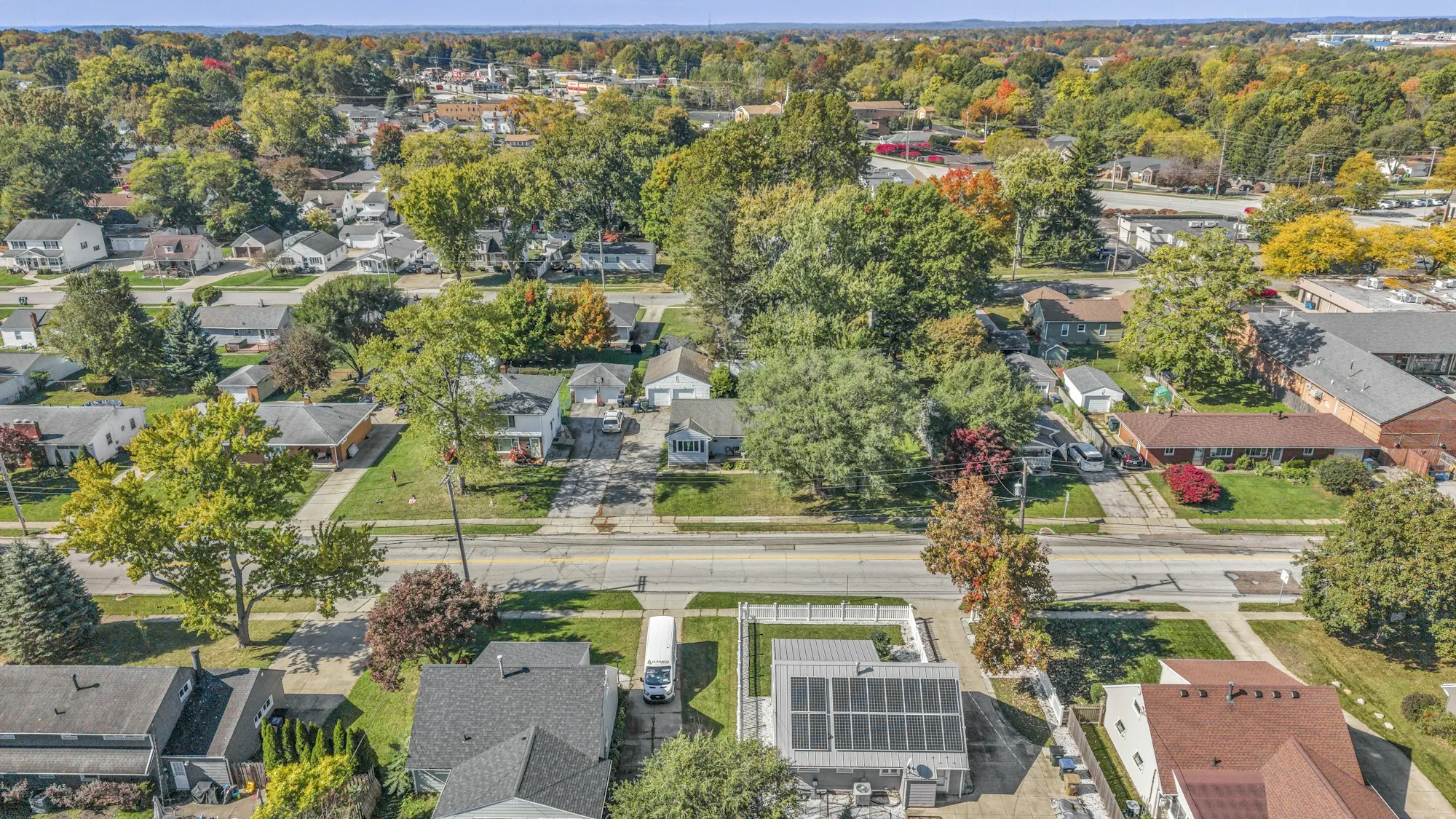 Aerial view of a tree-lined suburban neighborhood in fall with solar panels on a few roofs